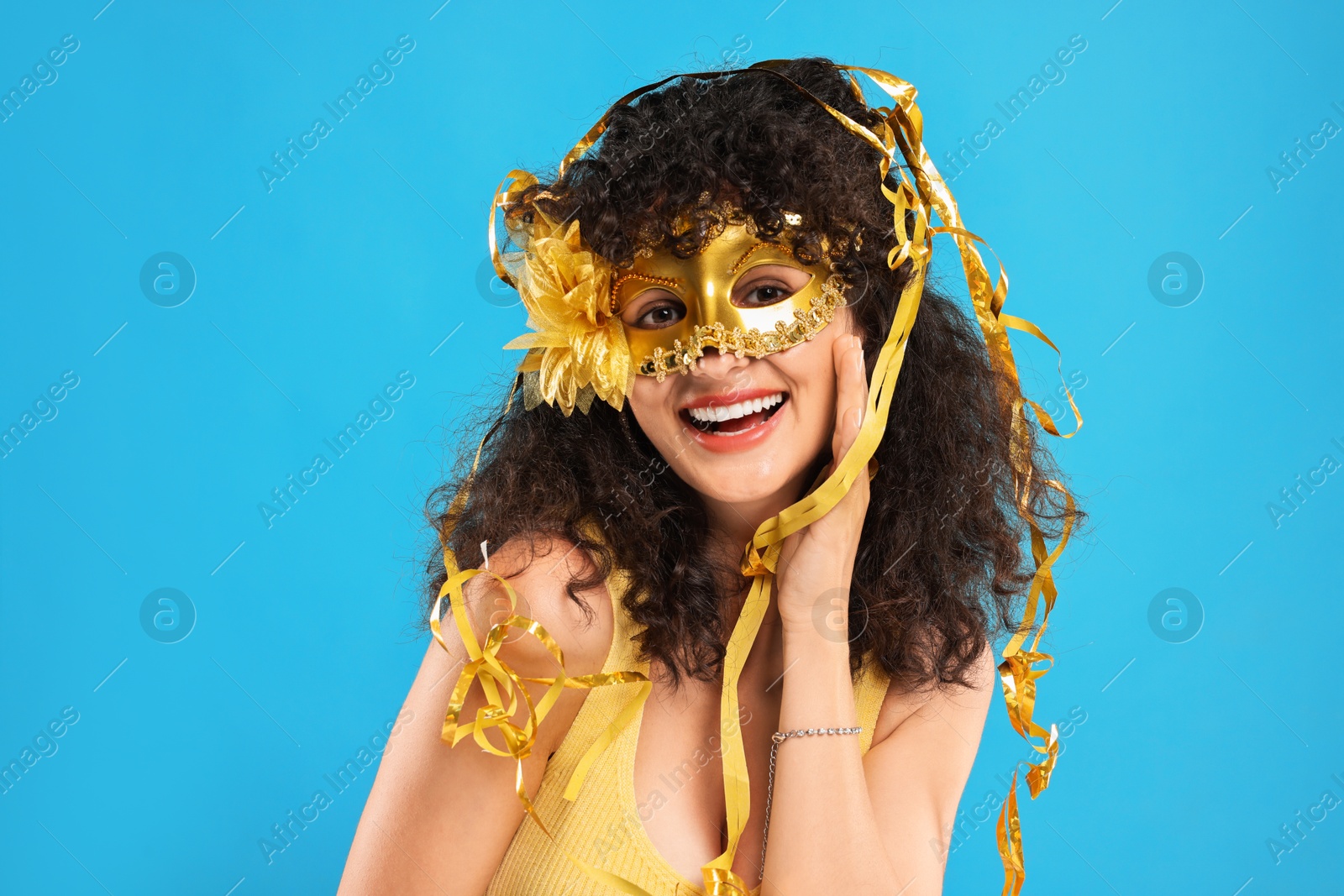 Photo of Happy young woman wearing carnival mask and tinsel on light blue background