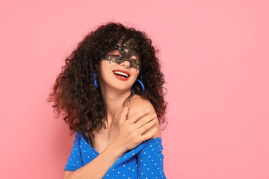 Happy young woman wearing carnival mask on pink background, space for text