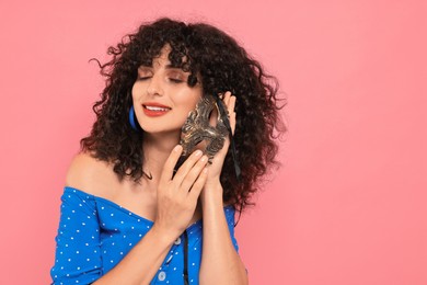 Smiling young woman with carnival mask on pink background, space for text