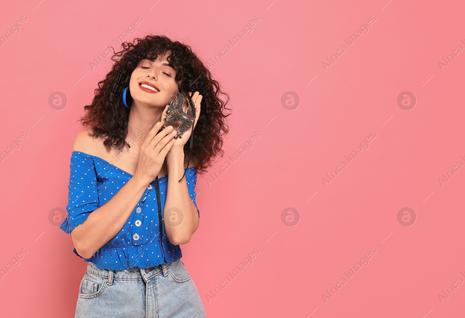 Photo of Smiling young woman with carnival mask on pink background, space for text