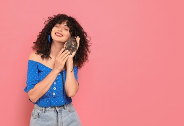 Smiling young woman with carnival mask on pink background, space for text