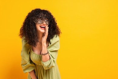 Happy young woman wearing carnival mask on yellow background, space for text