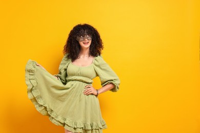 Photo of Happy young woman wearing carnival mask on yellow background, space for text