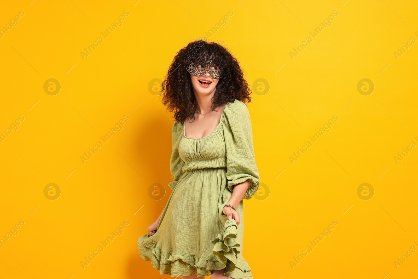 Photo of Happy young woman wearing carnival mask on yellow background