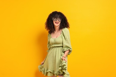 Happy young woman wearing carnival mask on yellow background