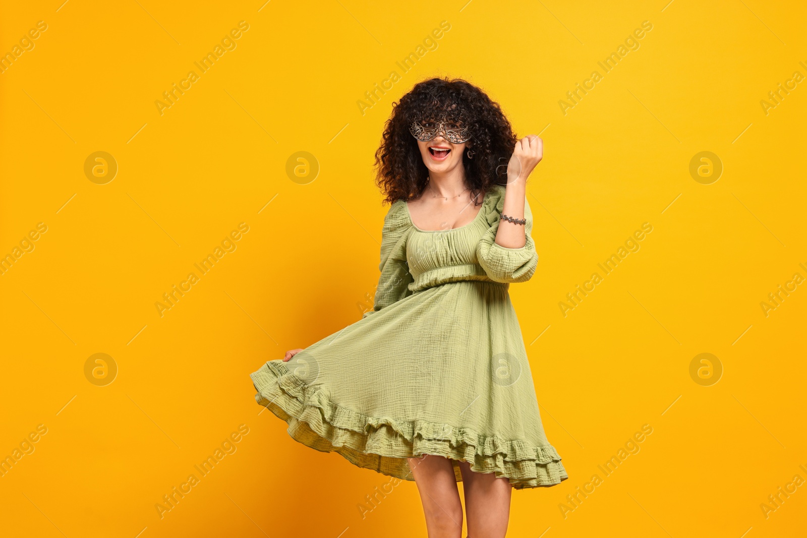 Photo of Happy young woman wearing carnival mask on yellow background