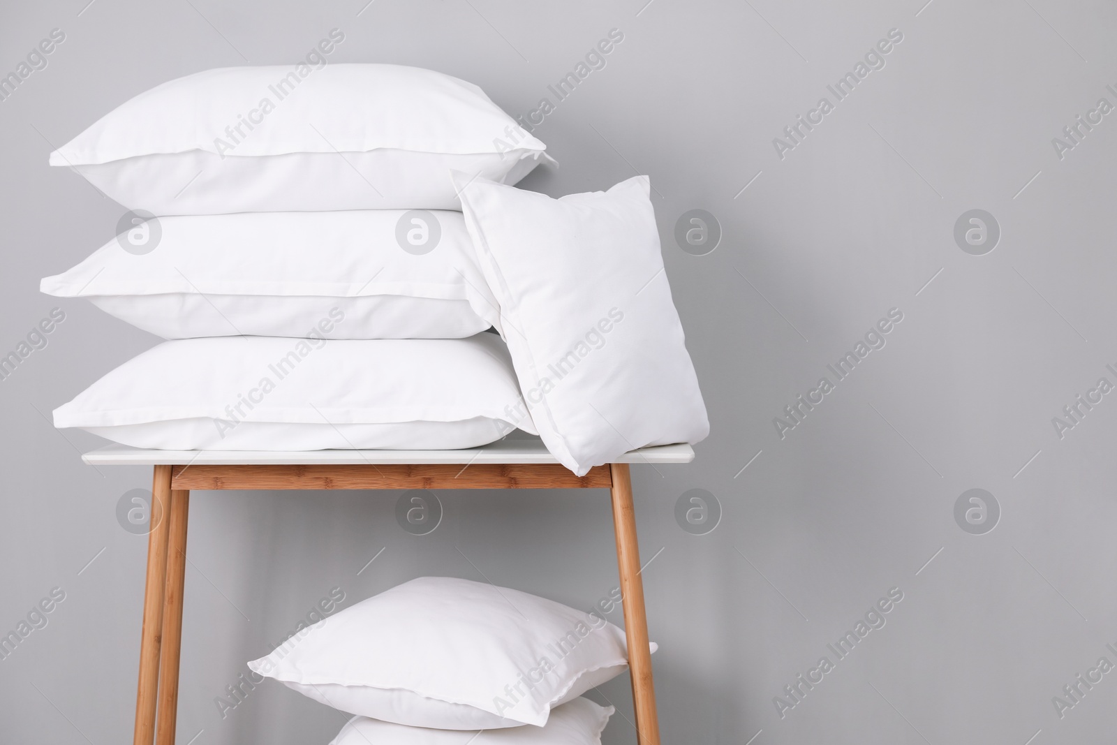 Photo of Stack of pillows on bench against grey wall. Space for text