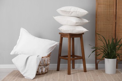 Photo of Stack of pillows, stool, storage basket and houseplant on floor indoors