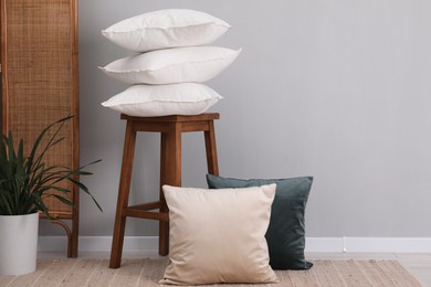 Photo of Stack of pillows, stool and houseplant on floor indoors