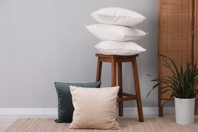 Photo of Stack of pillows, stool and houseplant on floor indoors