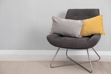 Photo of Soft armchair with pillows on floor indoors. Space for text