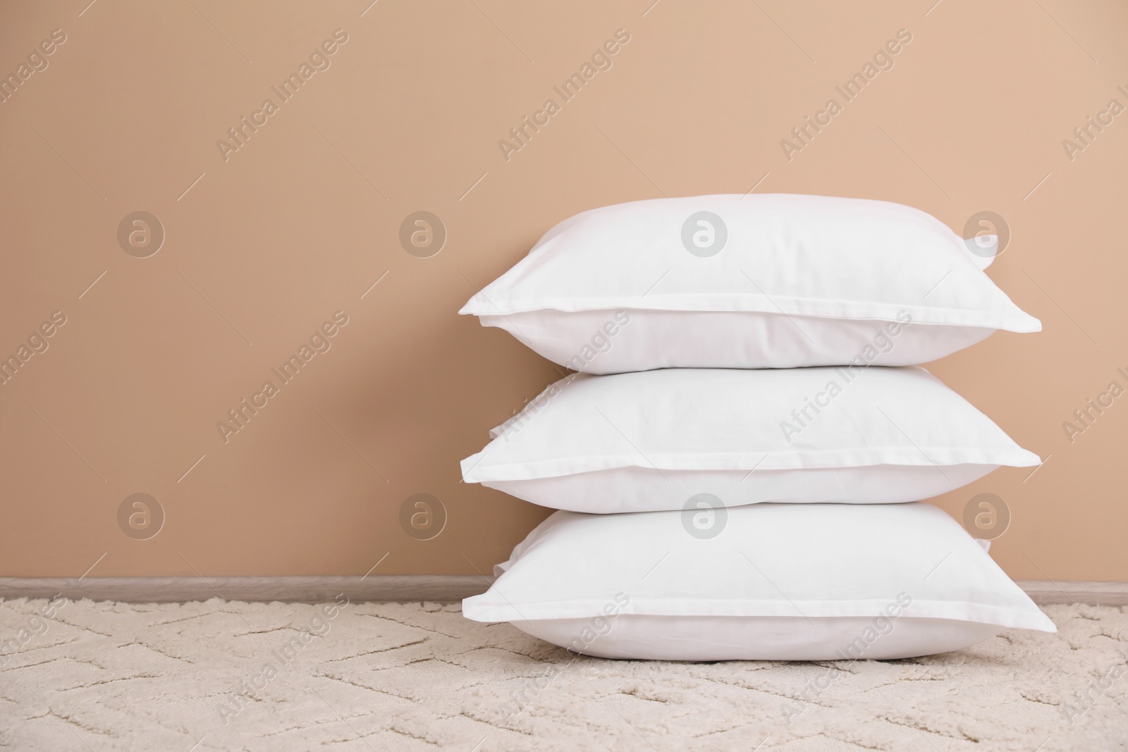 Photo of Stack of white pillows on floor near beige wall. Space for text