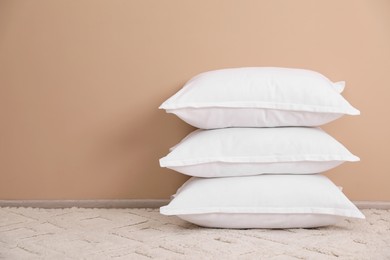 Photo of Stack of white pillows on floor near beige wall. Space for text