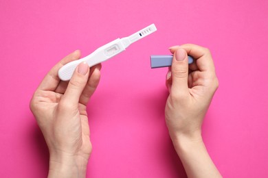 Photo of Woman holding pregnancy test on pink background, top view