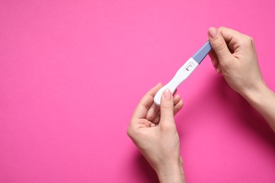 Photo of Woman holding pregnancy test on pink background, top view. Space for text