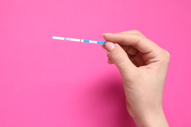 Photo of Woman holding pregnancy test on pink background, top view