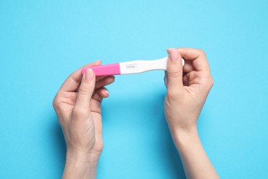 Woman holding pregnancy test on light blue background, top view