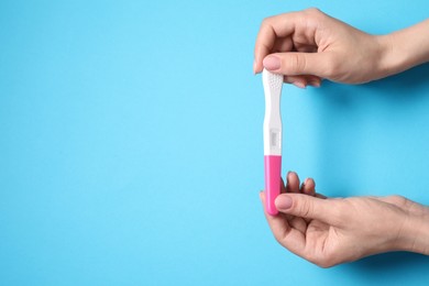 Woman holding pregnancy test on light blue background, top view. Space for text