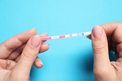 Woman holding pregnancy test on light blue background, top view