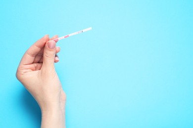 Photo of Woman holding pregnancy test on light blue background, top view. Space for text