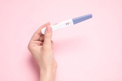 Woman holding pregnancy test on pink background, top view. Space for text