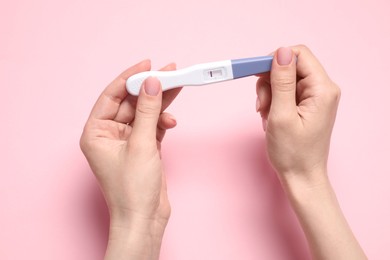 Photo of Woman holding pregnancy test on pink background, closeup