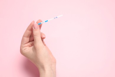 Woman holding pregnancy test on pink background, top view. Space for text