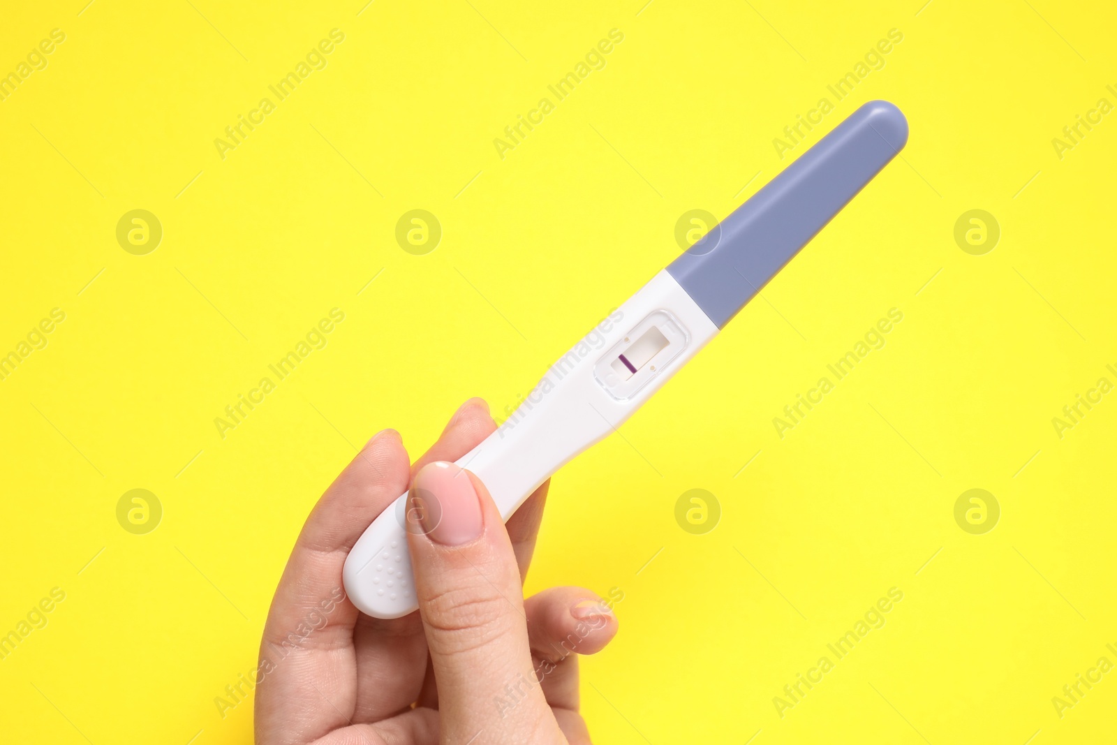 Photo of Woman holding pregnancy test on yellow background, closeup