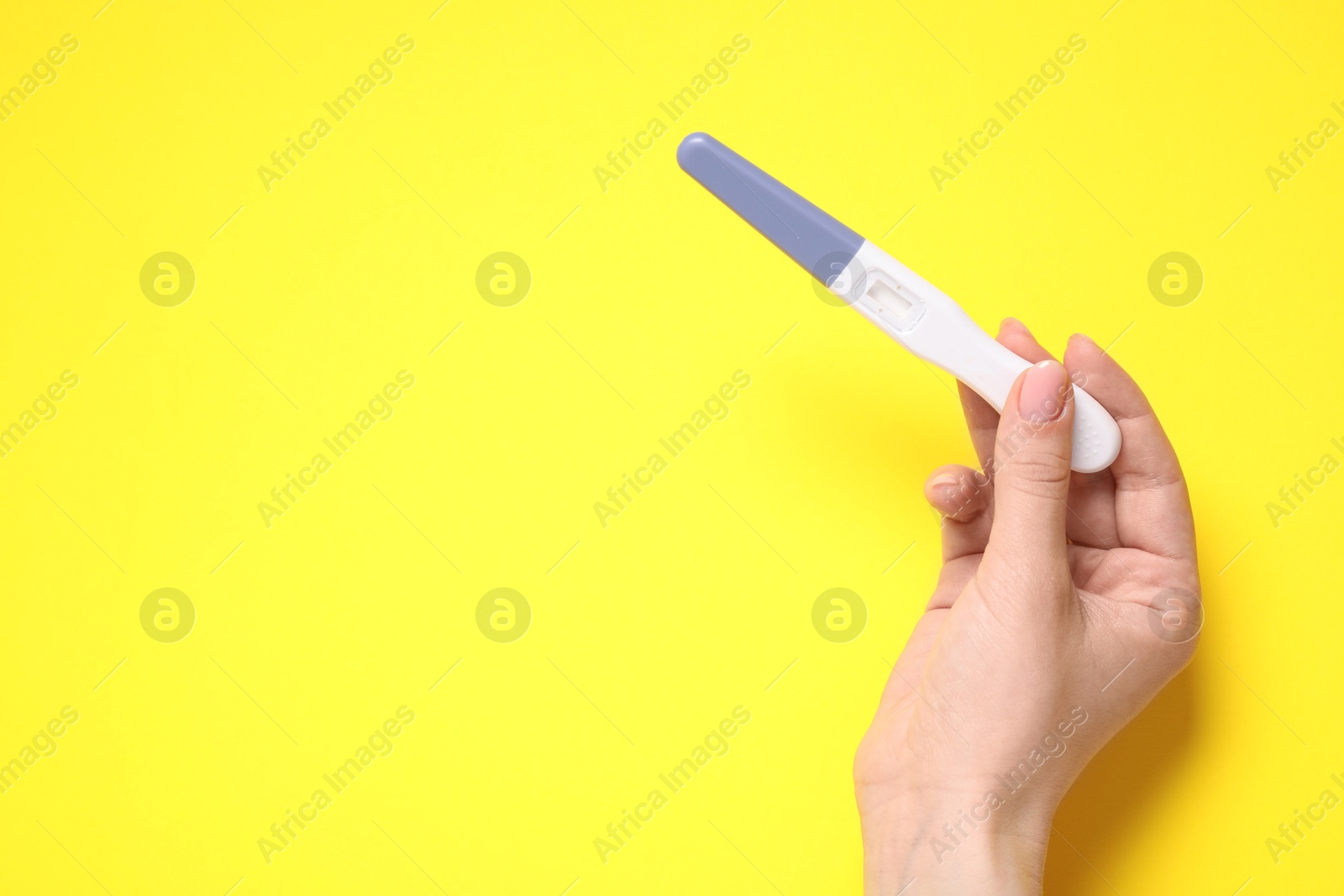 Photo of Woman holding pregnancy test on yellow background, closeup. Space for text