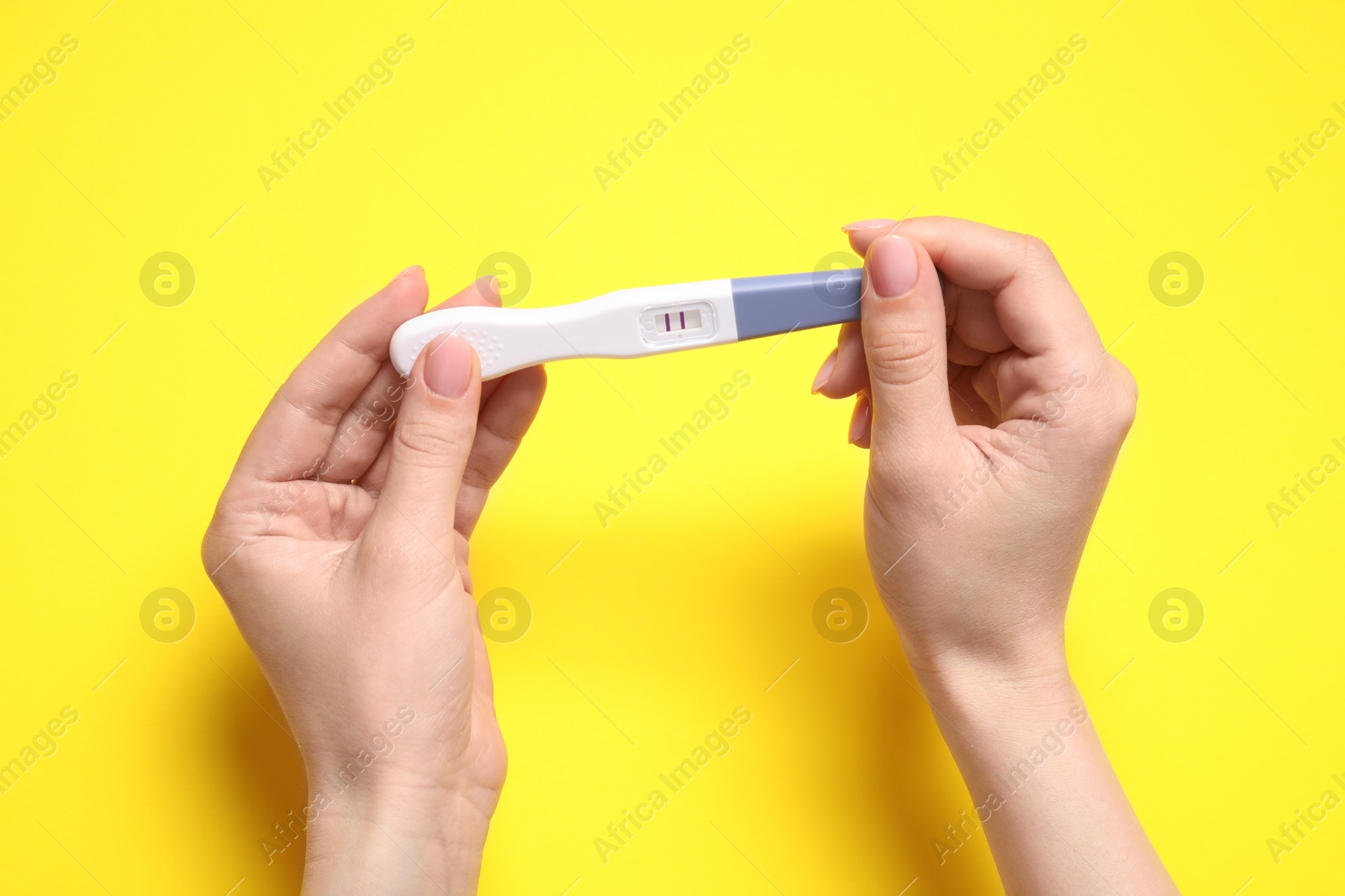 Photo of Woman holding pregnancy test on yellow background, closeup