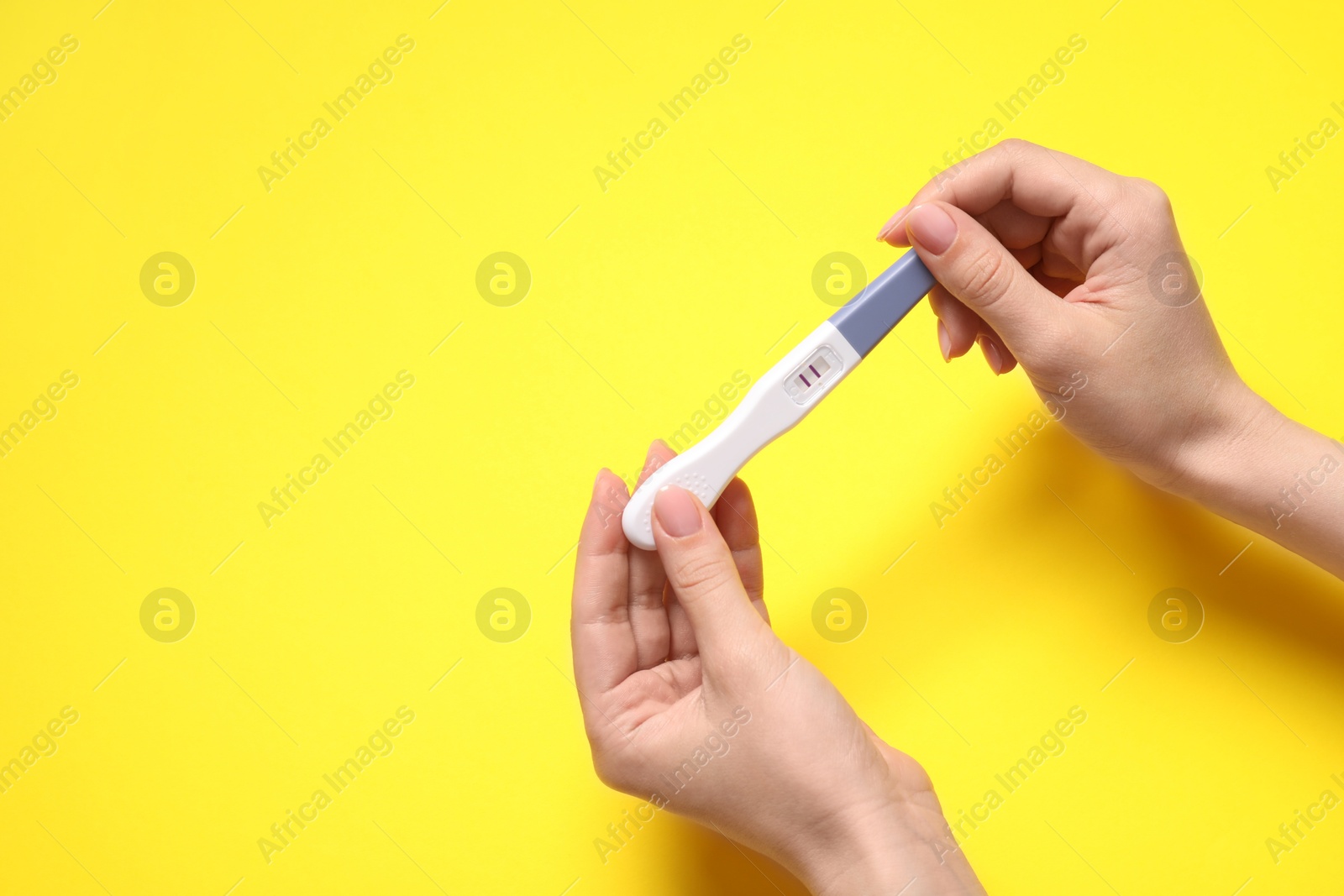 Photo of Woman holding pregnancy test on yellow background, closeup. Space for text