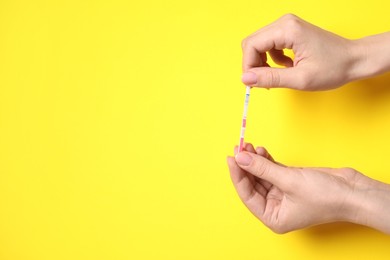 Woman holding pregnancy test on yellow background, top view. Space for text