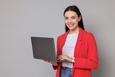 Beautiful woman in red jacket with laptop on gray background