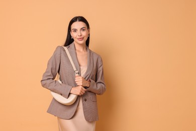 Beautiful woman in stylish jacket with bag on pale orange background, space for text