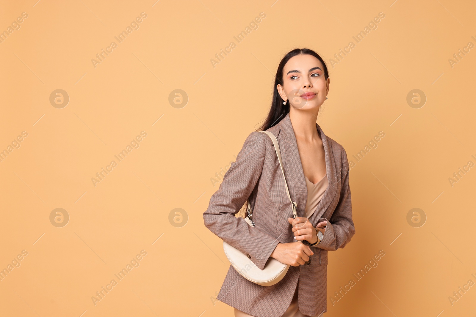 Photo of Beautiful woman in stylish jacket with bag on pale orange background, space for text