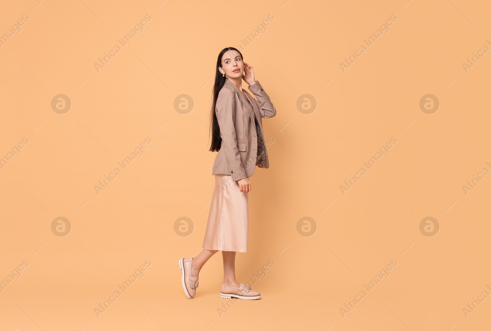 Photo of Beautiful woman in stylish jacket and beige dress on pale orange background