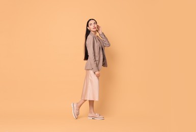 Photo of Beautiful woman in stylish jacket and beige dress on pale orange background