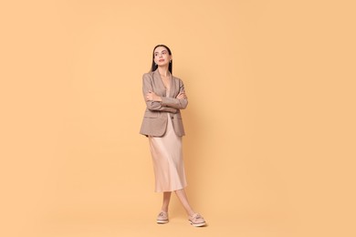 Photo of Beautiful woman in stylish jacket and beige dress on pale orange background