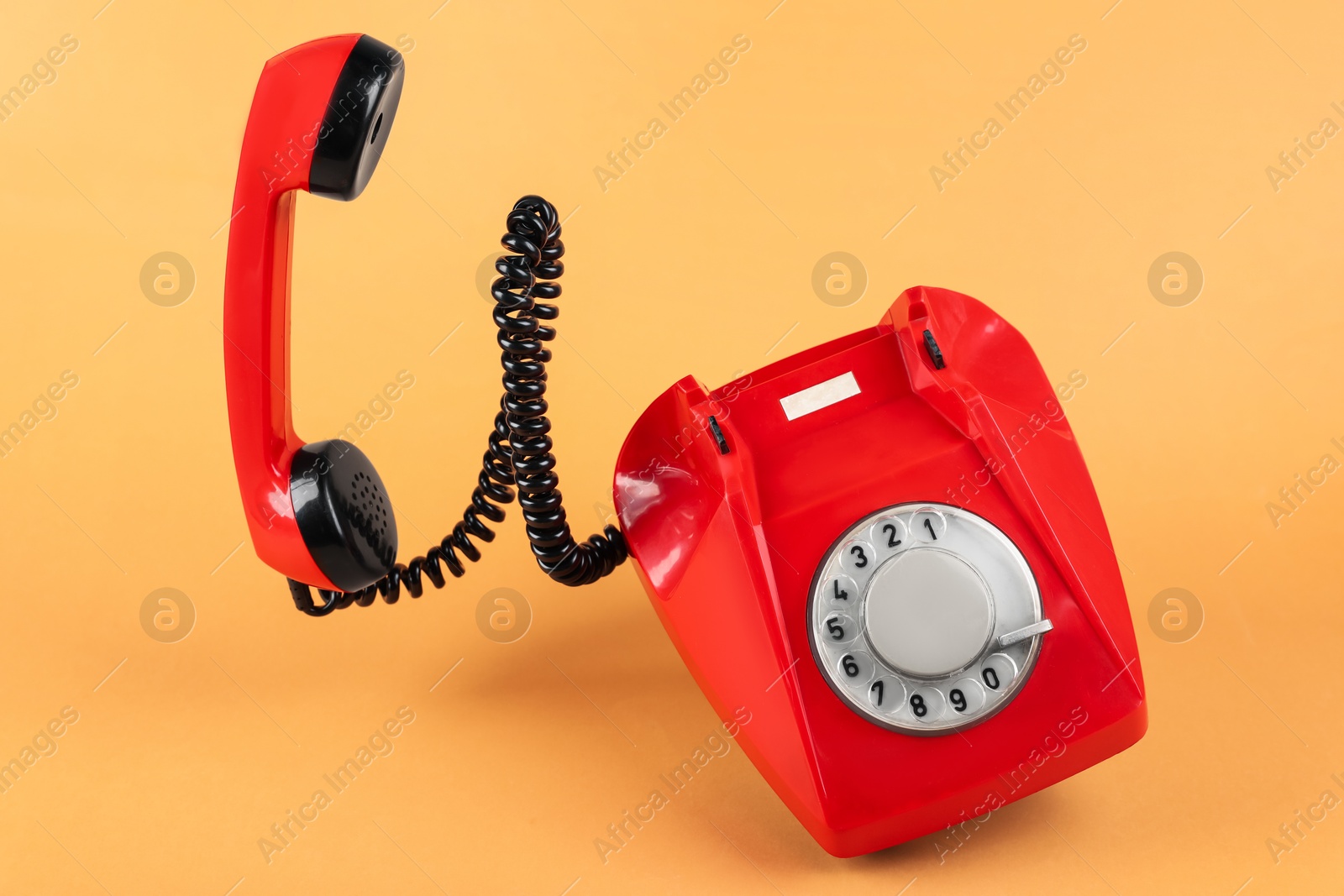 Photo of One red telephone with handset on pale orange background