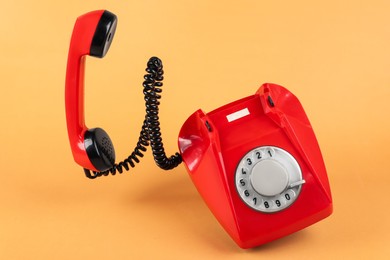 Photo of One red telephone with handset on pale orange background