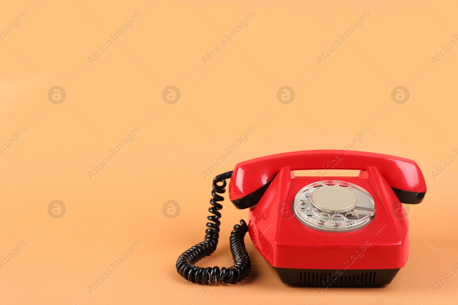 Photo of One red telephone with handset on pale orange background, space for text