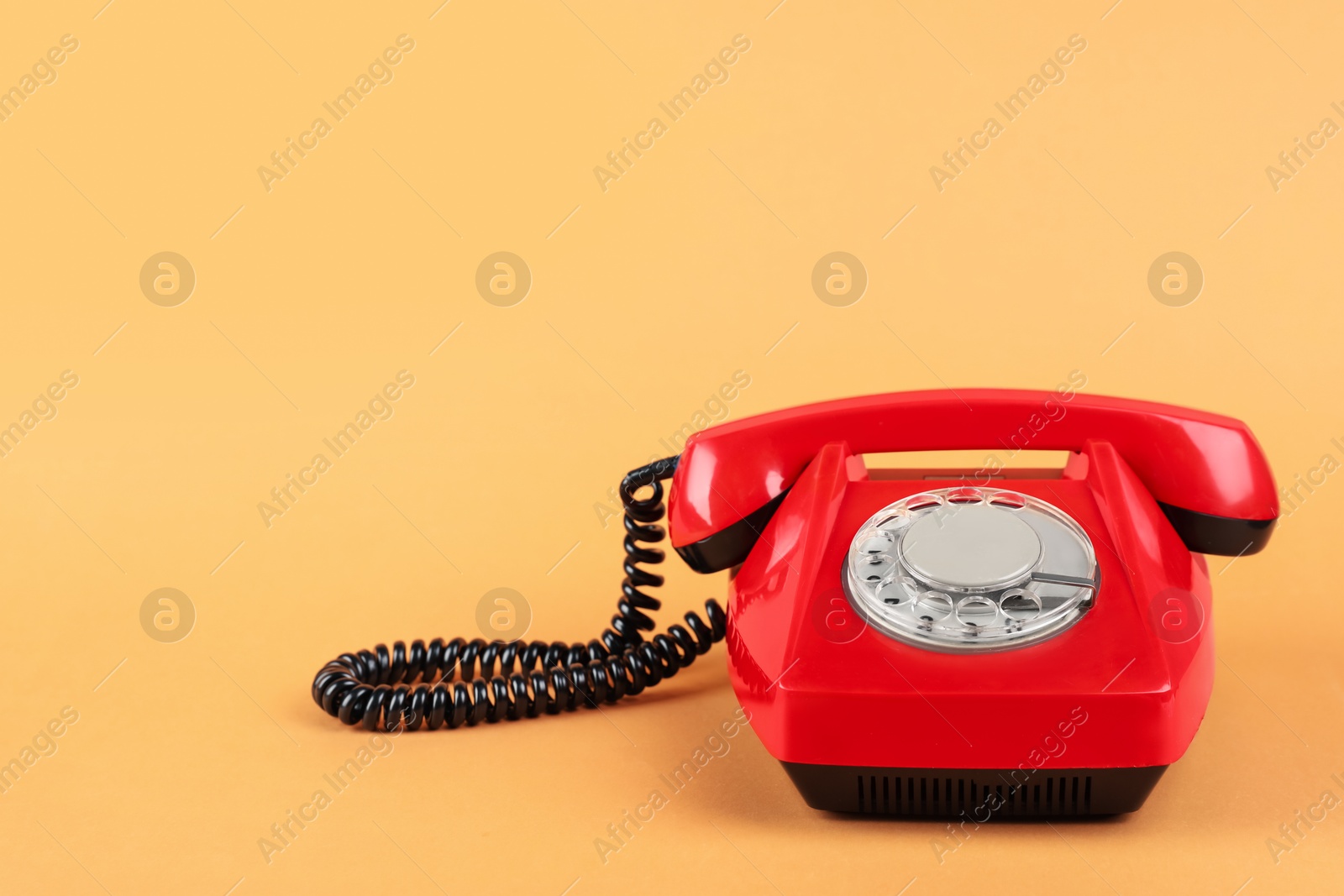 Photo of One red telephone with handset on pale orange background, space for text