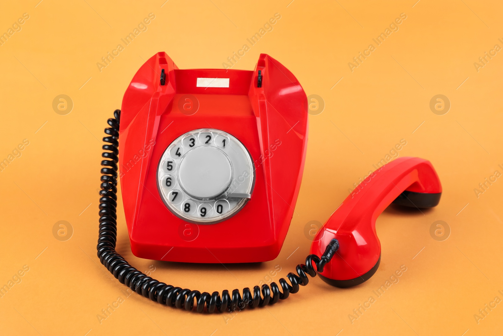 Photo of One red telephone with handset on pale orange background