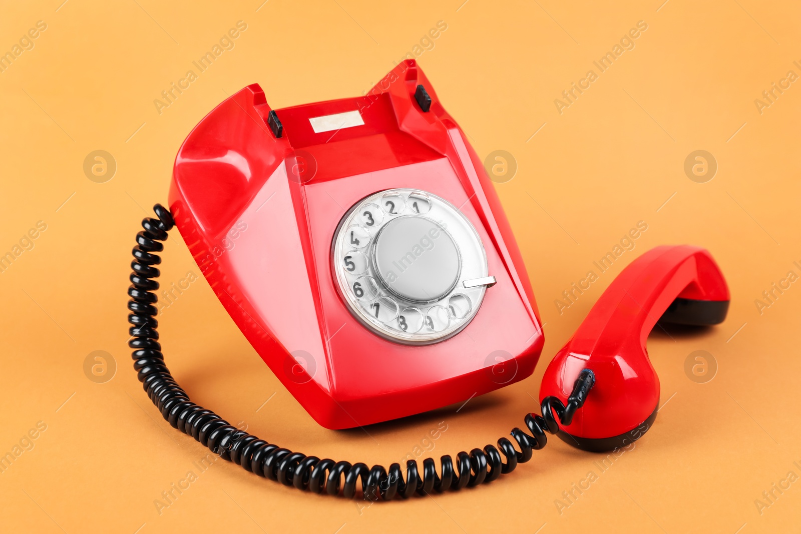 Photo of One red telephone with handset on pale orange background