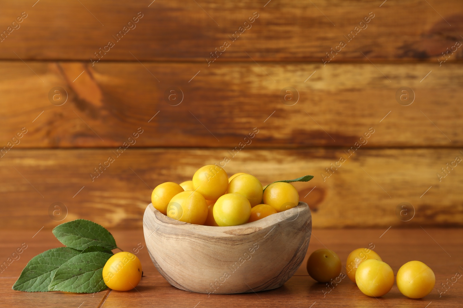 Photo of Ripe plums in bowl and leaves on wooden table