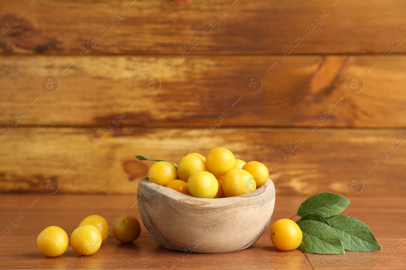 Photo of Ripe plums in bowl and leaves on wooden table