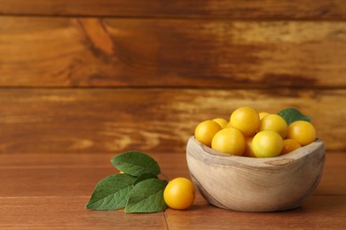 Photo of Ripe plums in bowl and leaves on wooden table