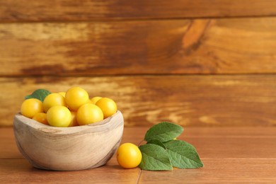 Photo of Ripe plums in bowl and leaves on wooden table, space for text