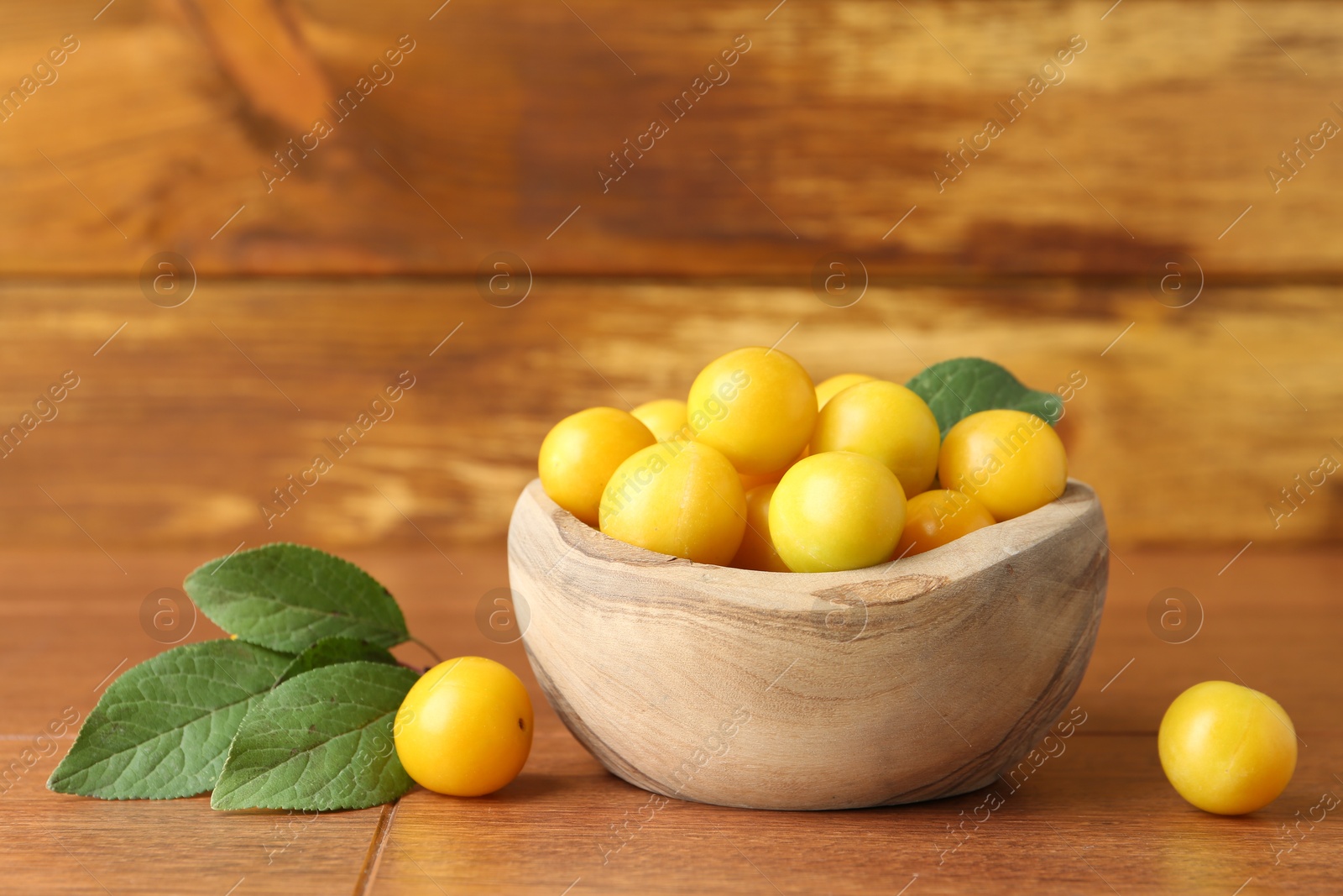 Photo of Ripe plums in bowl and leaves on wooden table