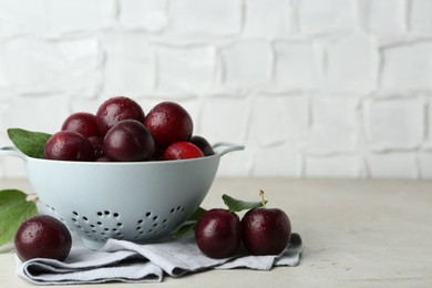 Photo of Ripe plums in colander and leaves on light textured table, space for text